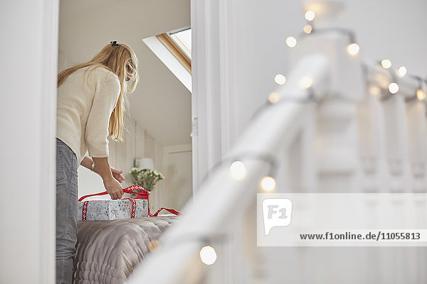 Eine Frau wickelt auf einem Bett rote Bänder um Weihnachtsgeschenke  Blick durch die Schlafzimmertür.