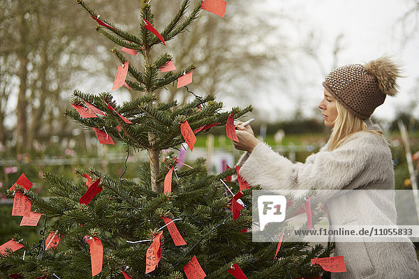 A woman reading handwritten red labels tied to the branches of a Christmas tree.