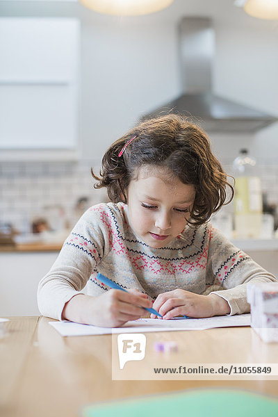 Ein Mädchen sitzt an einem Küchentisch und schreibt eine Karte oder einen Brief.