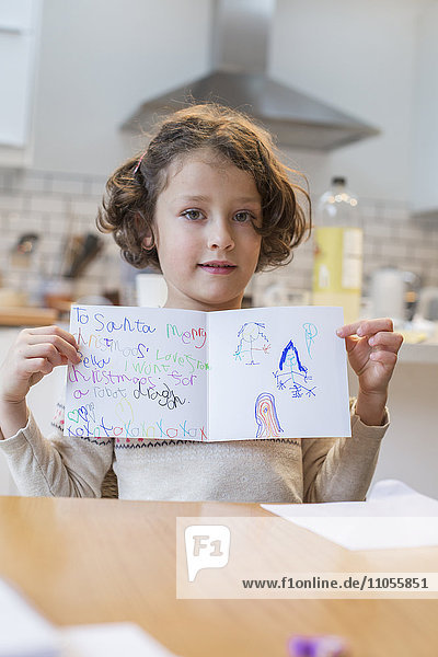 A girl showing her home made Christmas card  a letter to Santa Claus  with drawings and writing.