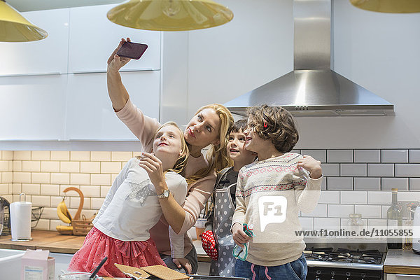 An adult woman and three children taking a selfy photograph in the kitchen.