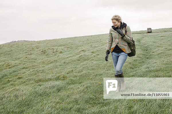 A woman in warm coat and gloves walking across open country  grassland and moors.