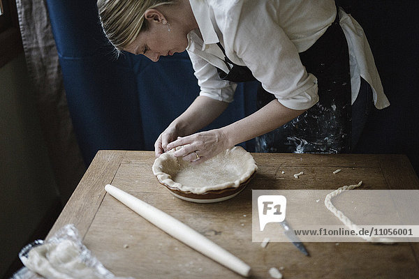 Eine Frau arbeitet daran  den Rand einer Konditoreihülle zu glätten  die eine Kuchenform auskleidet.