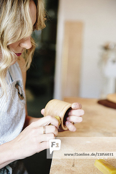 Eine Frau in einer Werkstatt  die eine Wachsplatte benutzt  um eine kleine holzgedrechselte Tasse oder Schale zu ölen.