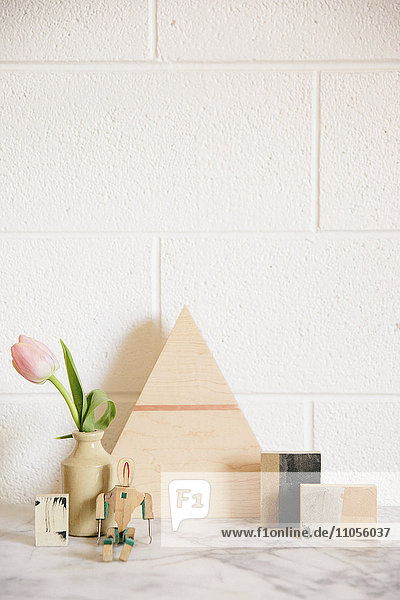 Eine steinerne Arbeitsplatte mit einem hölzernen Dreieck aus Holz,  kleinen Holzwürfeln und einer rosa Tulpe in einem Glas.