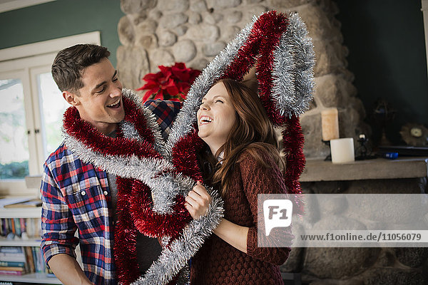 Ein junges Paar hängt Lametta auf und schmückt zu Weihnachten ein Haus.