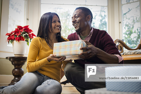 A couple on a sofa  exchanging wrapped presents.