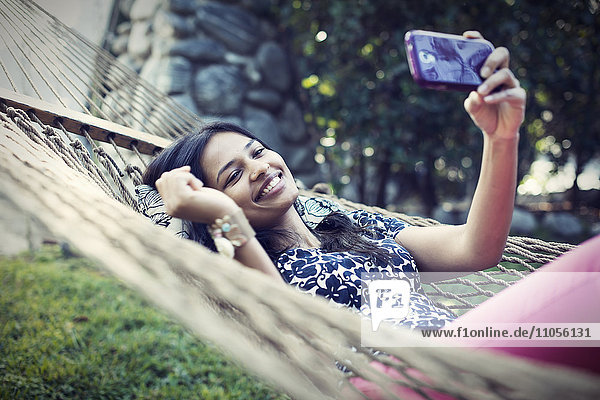 A woman lying in a garden hammock taking selfies with her phone.