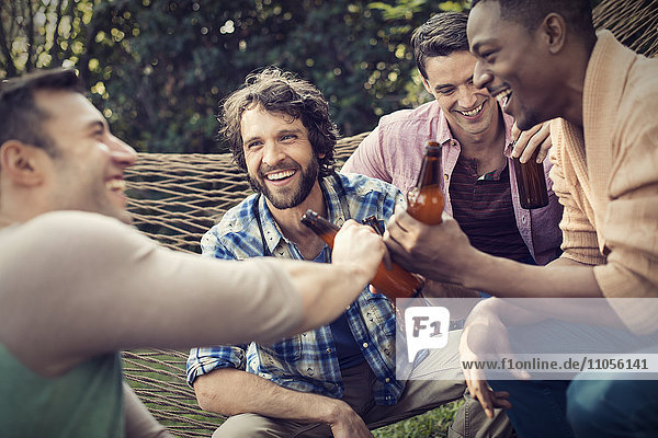 A group of friends lounging in a large hammock in the garden having a beer.