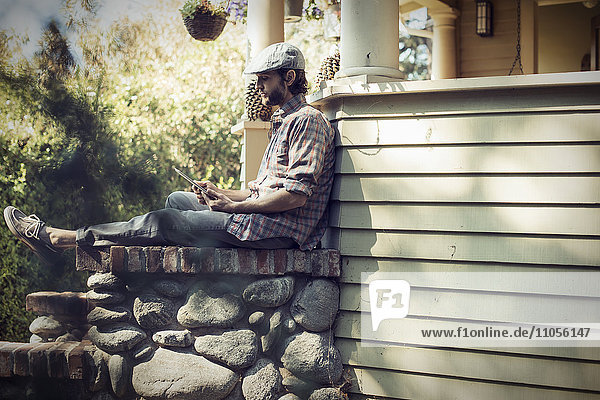 Ein Mann sitzt entspannt in einer ruhigen Ecke einer Veranda und benutzt ein digitales Tablet.