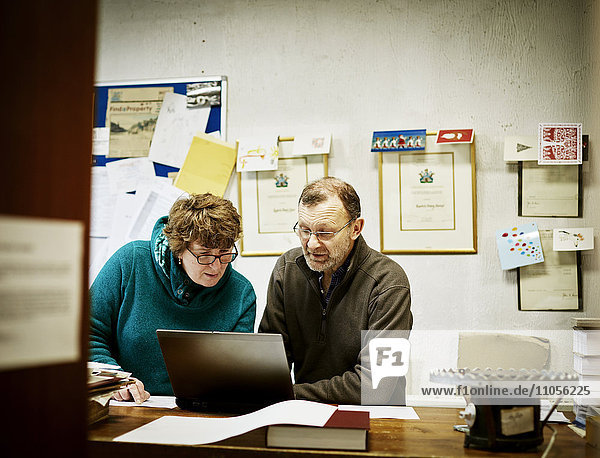Zwei Personen an einem Computer in einem kleinen Buchbindereibetrieb.