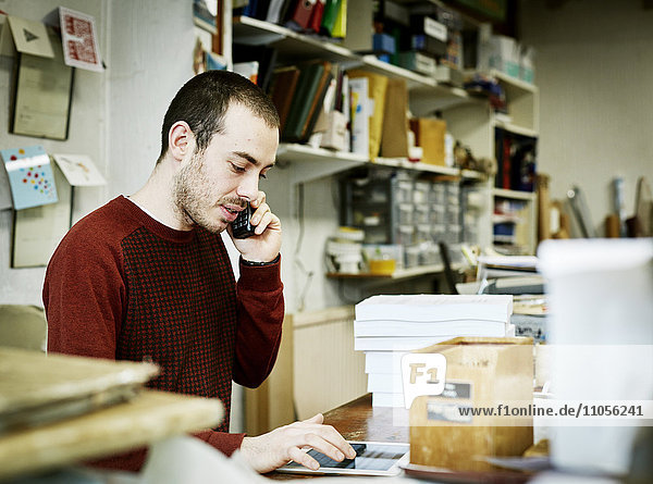 Ein Mann mit einem Smartphone und einem digitalen Tablet in einer kleinen Buchbinderei.