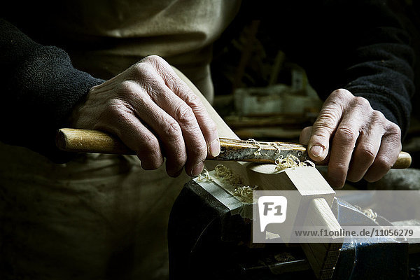 Ein Mann  der in der Werkstatt eines Möbelherstellers arbeitet und eine Raspel an einem Stück Holz in einer Klemme benutzt.