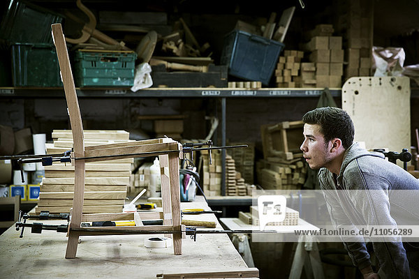 Ein Mann  der in der Werkstatt eines Möbelherstellers arbeitet und einen Stuhl zusammenbaut.
