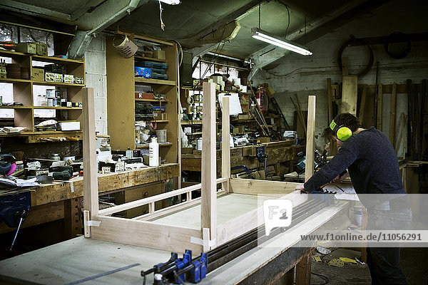 Ein Mann  der in der Werkstatt eines Möbelherstellers arbeitet und einen Tisch zusammenbaut.