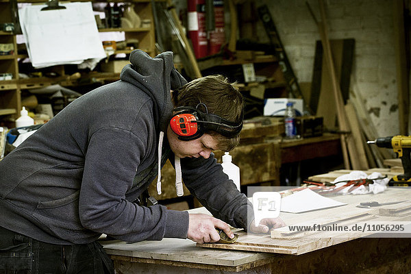Ein Mann  der in der Werkstatt eines Möbelherstellers arbeitet  trägt Ohrenschützer und benutzt einen scharfen Meißel auf Holz.