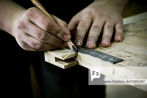 Ein Mann  der auf Holz arbeitet  eine Fuge oder Ecke mit Lineal und Bleistift misst.