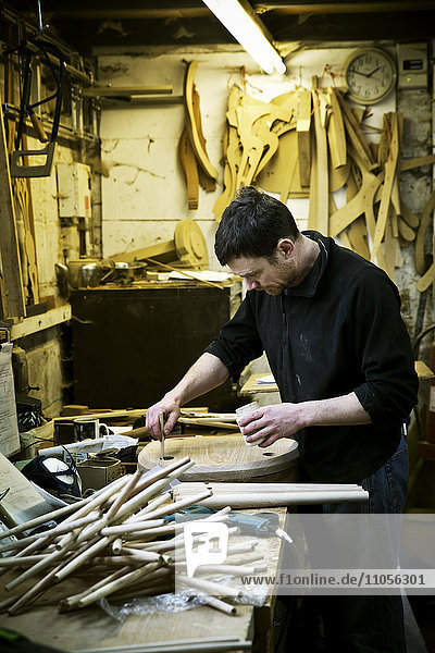 Ein Mann  der in der Werkstatt eines Möbelherstellers arbeitet. Stuhlbeine auf der Bank.