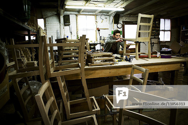 Ein Mann  der in der Werkstatt eines Möbelherstellers arbeitet und einen Stuhl zusammenbaut.