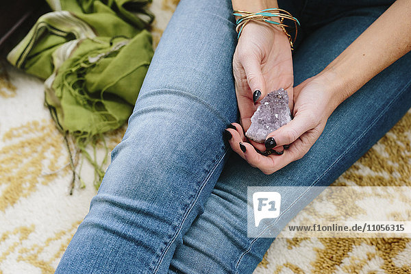 A woman sitting holding a small purple crystal in her hands.