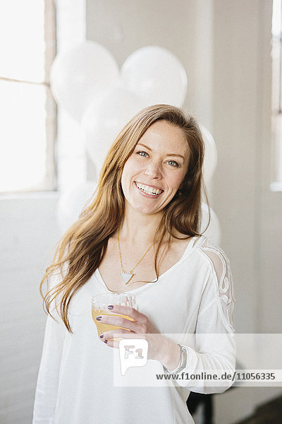 A woman with long hair in a white blouse  holding a drink. White balloons  party decorations.