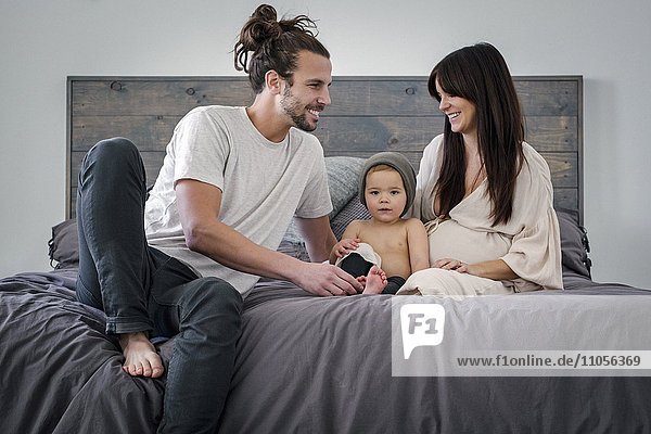 A young couple and their young son sitting together on their bed.