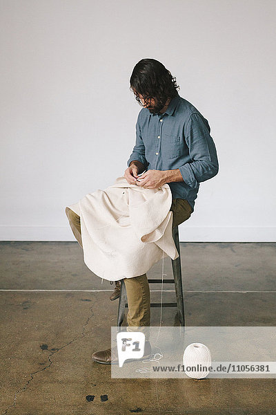 Ein Mann sitzt auf einem Hocker und verwendet Schnur- und Handarbeitstechniken  um ein Kunstwerk zu schaffen.