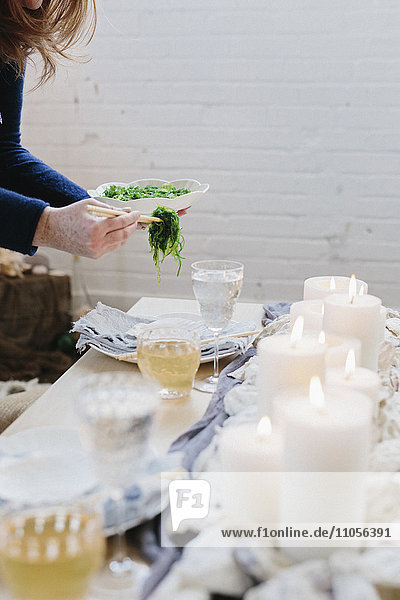 Eine Frau stellt einen Teller mit Essen auf einen mit brennenden Kerzen dekorierten Tisch.