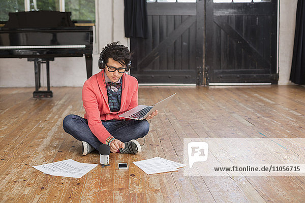 Young man sitting on the floor in a rehearsal studio  using a laptop computer  looking at sheet music.