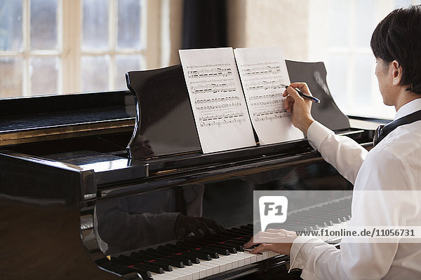 Young man sitting at a grand piano in a rehearsal studio  annotating sheet music.