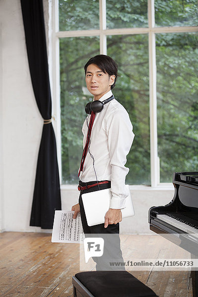 Young man standing next to a grand piano in a rehearsal studio  holding sheet music.