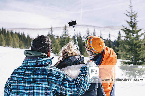 Drei Personen  zwei Männer und eine junge Frau in Skiausrüstung  posieren für einen Selfie  einer hält einen Selfie-Stock.