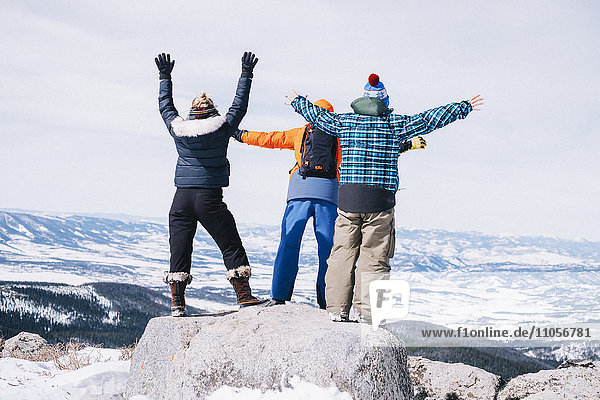 Three people  two men and a young woman standing on top of a mountain with arms outstretched.