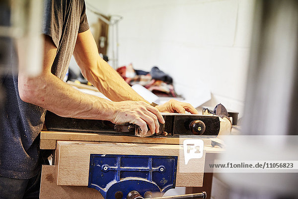 Eine Möbelwerkstatt,  die maßgeschneiderte zeitgenössische Möbelstücke unter Verwendung traditioneller Fertigkeiten im modernen Design herstellt. Ein Mann,  der ein Stück Holz mit Knöpfen hält und an einer Werkbank arbeitet.