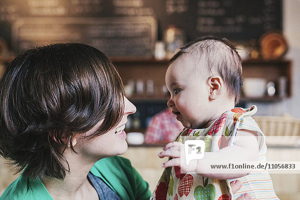 A mother and small baby gazing at each other and smiling  in a coffee shop.