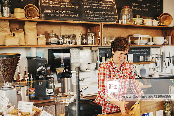 A woman in a plaid shirt working behind the counter in a coffee shop.