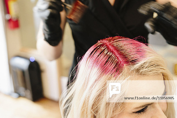 A hair colourist in gloves applying red hair dye to a client's blonde hair with a brush.