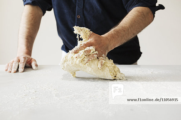 Nahaufnahme eines Bäckers  der Brotteig zu einem Laib knetet und formt.