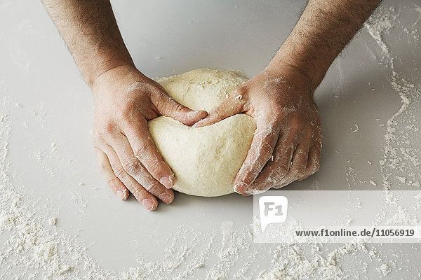 Nahaufnahme eines Bäckers  der Brotteig zu einer Kugel knetet und formt.