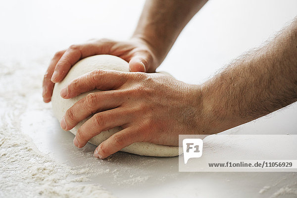 Nahaufnahme eines Bäckers  der eine Portion Brotteig knetet und zu einer Kugel formt.