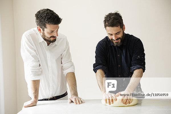 Two bakers standing at a table  kneading bread dough.