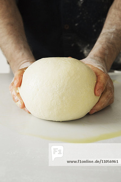 Nahaufnahme eines Bäckers  der einen großen Brotteig knetet und formt.