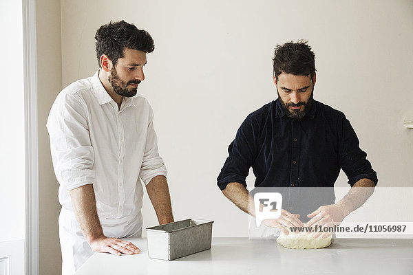 Zwei Bäcker  die an einem Tisch stehen und Brotteig kneten  eine Backform aus Metall.