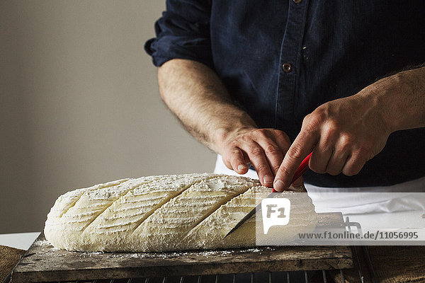 Nahaufnahme eines Bäckers  der mit einem Brotmesser einen frisch gebackenen Laib Brot schneidet.