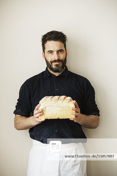 Bäcker hält einen Laib frisch gebackenes Weißbrot in der Hand.
