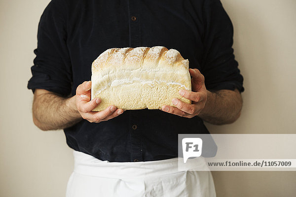 Nahaufnahme eines Bäckers  der einen frisch gebackenen Laib Weißbrot in der Hand hält.
