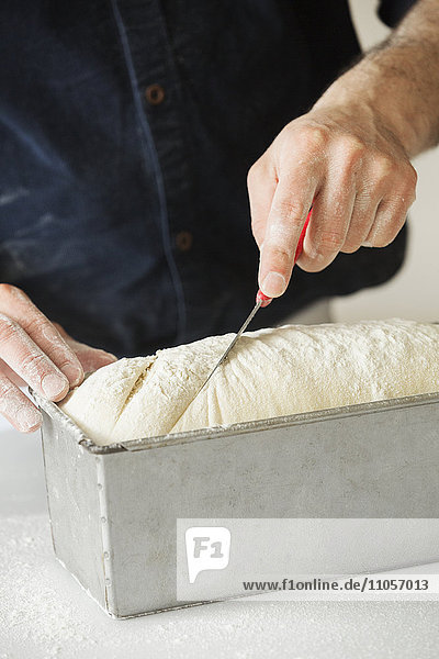 Nahaufnahme eines Bäckers  der Brotteig in einer Backform schneidet.
