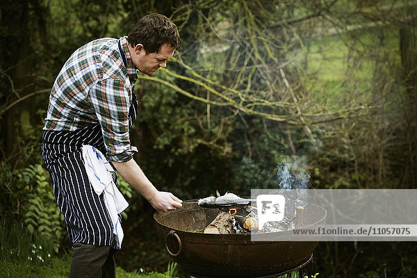 Chef standing in a garden  grilling a fish on a barbecue.