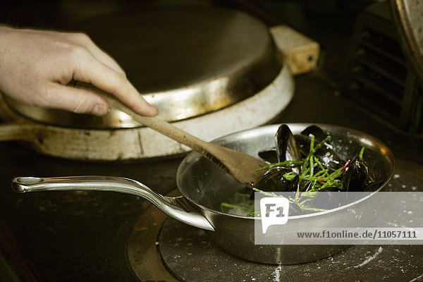 Chef stirring Black Mussels and samphire in a pan on a stove.