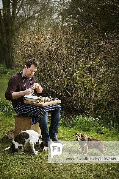 Chef sitting outdoors  preparing seafood  two dogs at his feet.